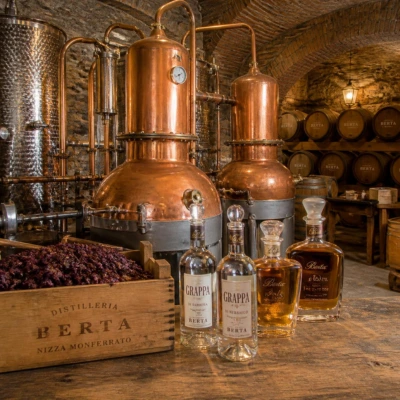 Maître distillateur travaillant devant des alambics en cuivre traditionnels et des fûts de vieillissement pour la fabrication de Grappa artisanale